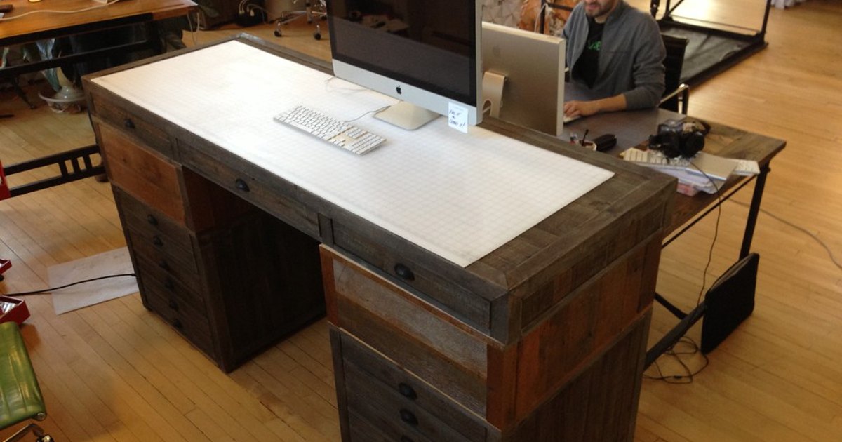 A wood standing desk holding a computer monitor and keyboard in a studio workspace.